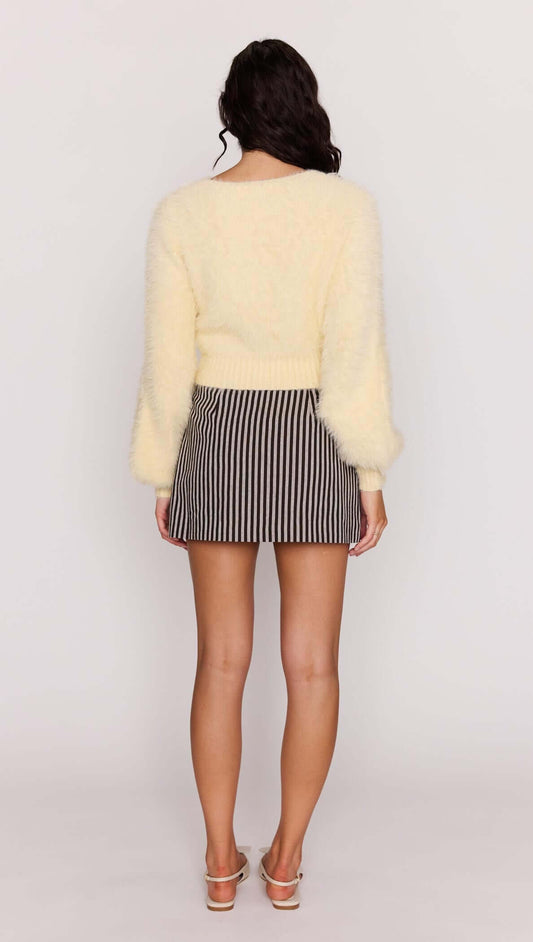 Back view of a woman wearing a Butter Yellow Fluffy Knit Jumper paired with a striped skirt.