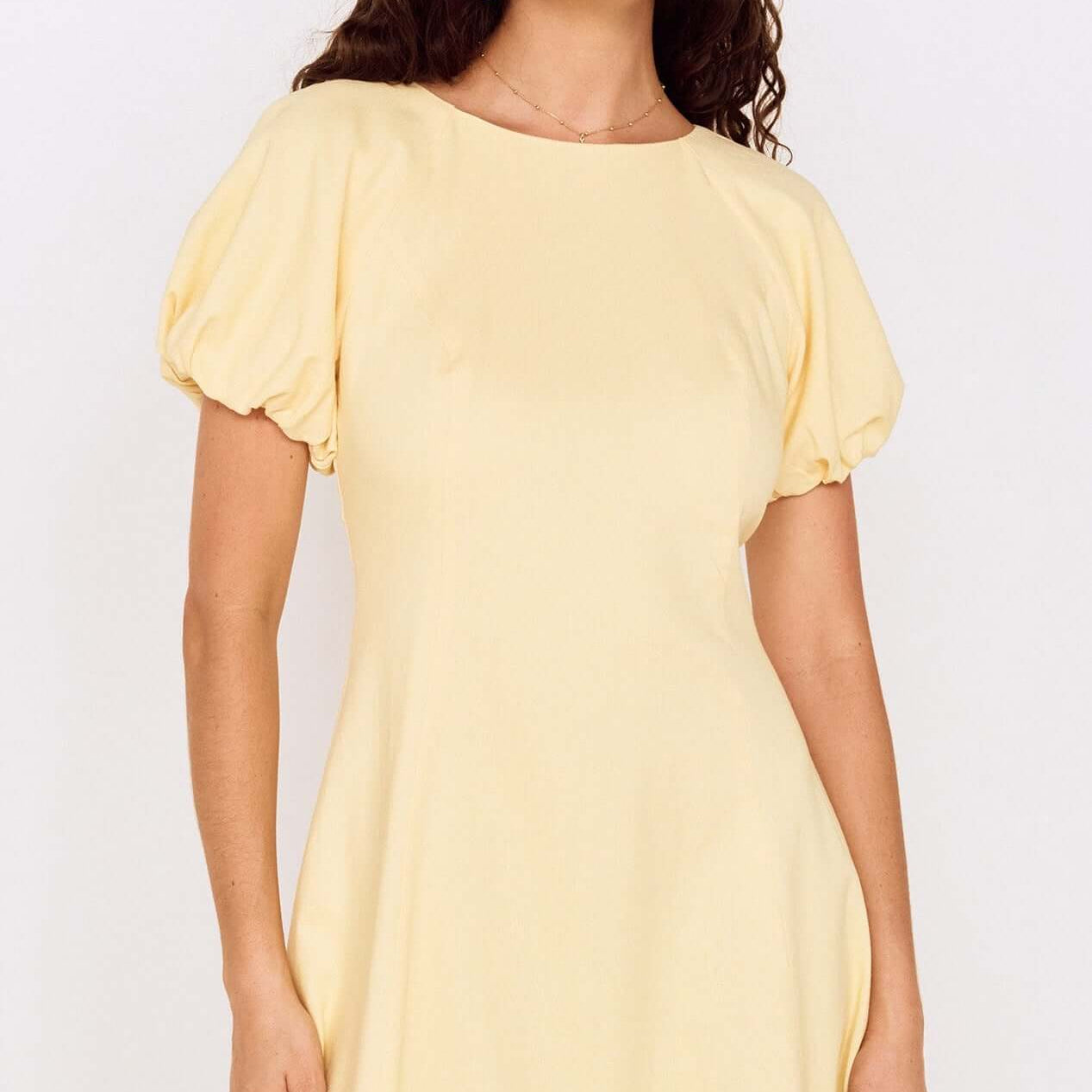 Butter Yellow Puff Sleeve Mini Dress displayed by a model with curly hair, showcasing a soft and feminine style.