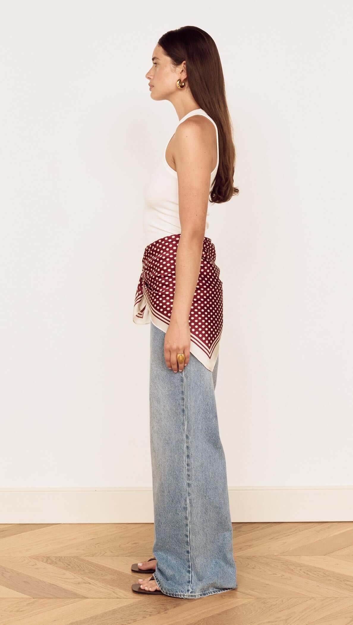 Woman wearing a Chocolate Polka Dot Scarf tied as a waist scarf, styled with relaxed denim jeans.
