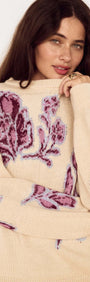 Model wearing a Cream Floral Intarsia Knit Sweater with floral motifs in wine and lilac, smiling at the camera.