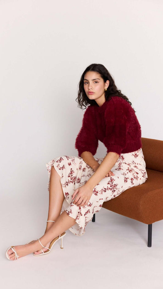 Model wearing a Cream Floral Toile Bias Cut Maxi Skirt paired with a burgundy sweater, seated on a stylish brown chair.
