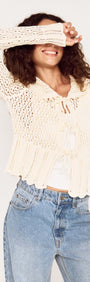 Model wearing a Cream Pointelle Knit Cardi with Tie Front, smiling and playfully covering her face.