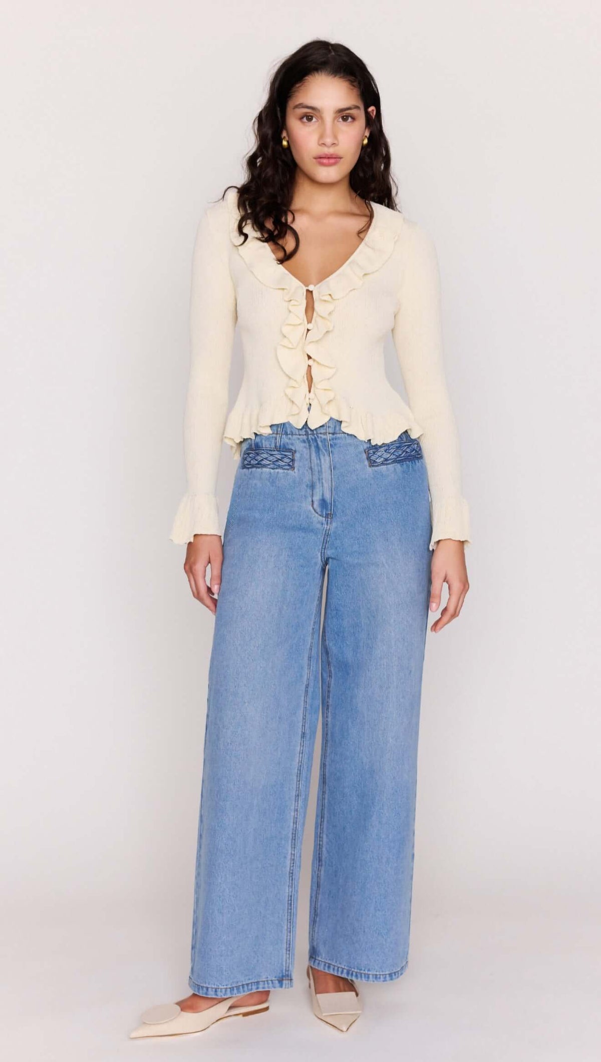 Model wearing a Cream Ruffled Cardigan with ruffle trim, paired with wide-leg jeans.