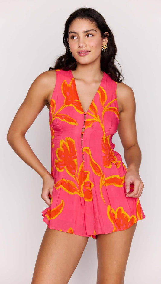 Model showcasing the ELODIE SLEEVELESS PLAYSUIT in vibrant pink with floral patterns.