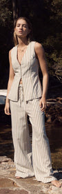 Model wearing an Olive & White Stripe Cotton Blend Vest paired with relaxed pants by MINKPINK at a coastal setting.