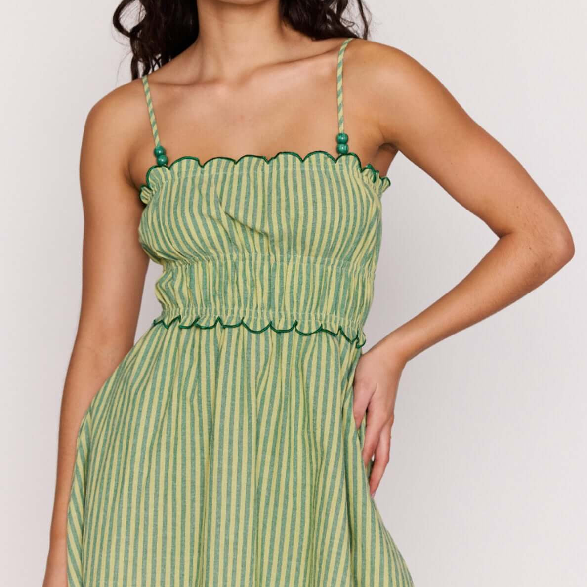 Playful model wearing the Green Striped Linen Blend Scallop Mini Dress with a flared mini skirt and scalloped edges.