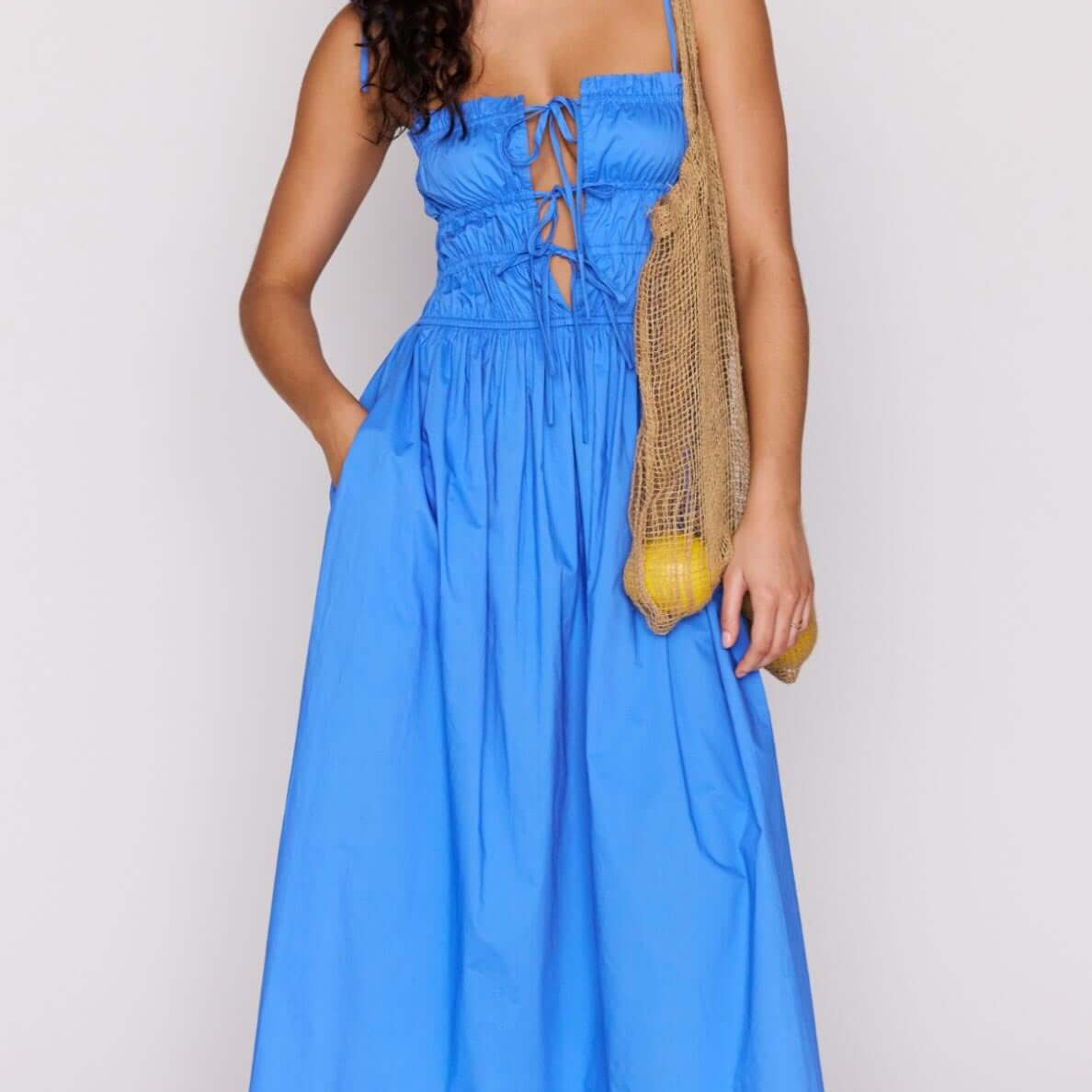Model wearing a blue cotton tie detail midi dress with a shirred bodice and adjustable tie detailing.