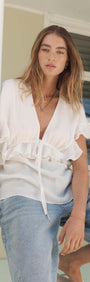 Model wearing the Marlon White Ruffle Blouse with flutter sleeves, paired with denim for a chic summer look.