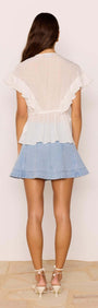 Back view of the Marlon White Ruffle Blouse styled with a denim skirt, showcasing flutter sleeves and ruffle detailing.
