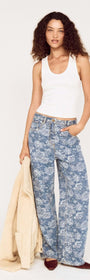 Woman wearing Mid Rise Floral Denim Wide Leg Jeans with a white tank top and beige jacket.