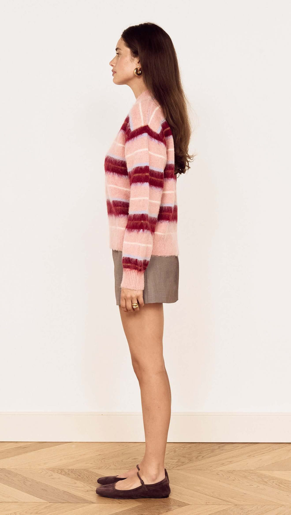 Young woman wearing a Pink Brushed Stripe Crew Neck Sweater with a relaxed fit and side view, styled over a mini skirt.
