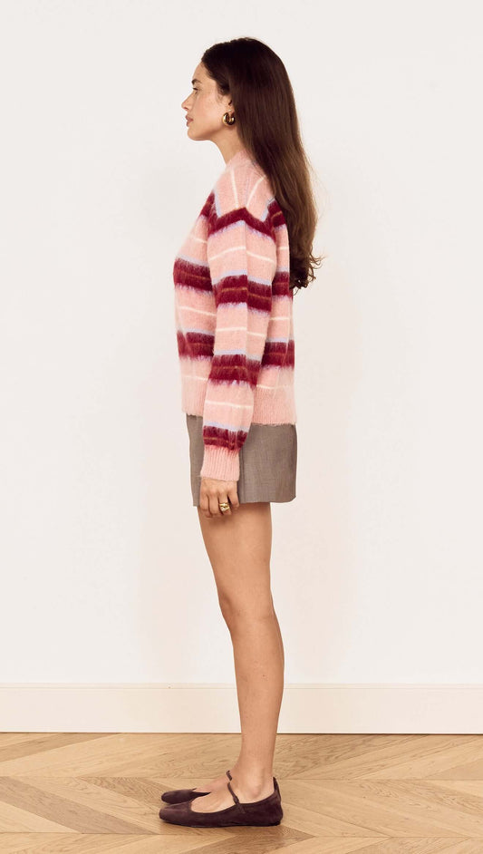 Young woman wearing a Pink Brushed Stripe Crew Neck Sweater with a relaxed fit and side view, styled over a mini skirt.