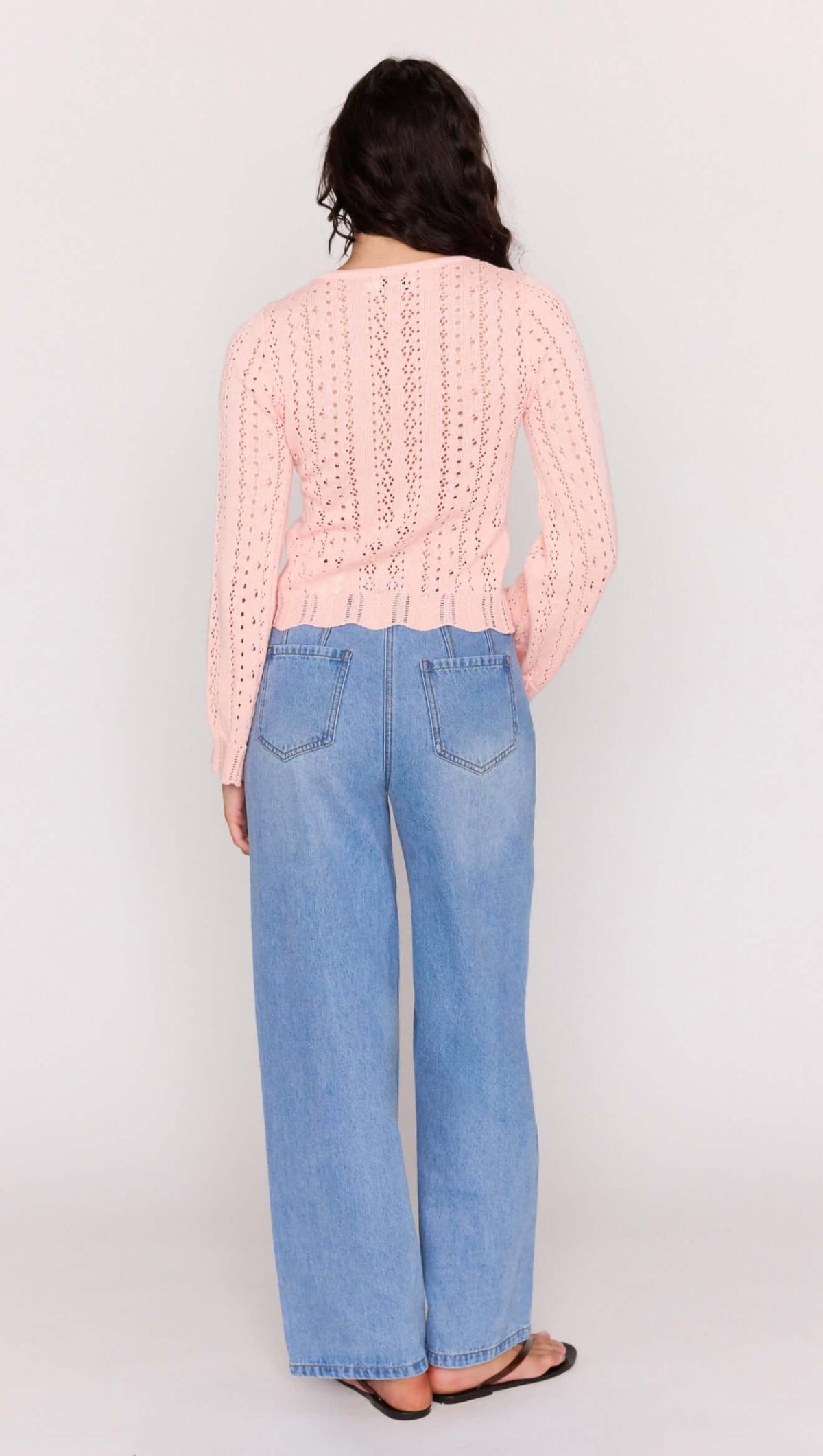 Soft Pink Cotton Pointelle Cardigan from the back, showcasing delicate pointelle knit and relaxed fit paired with wide-leg jeans.