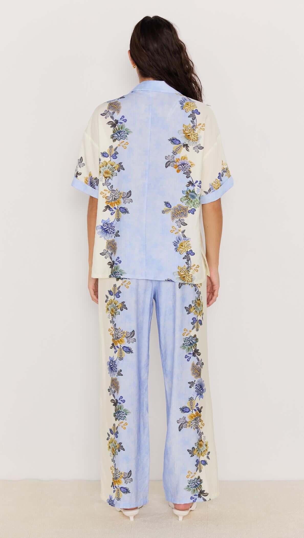Back view of woman wearing Lucia blue floral wide leg drawstring pants with matching floral shirt.