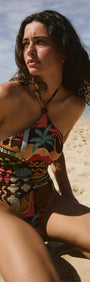 Woman wearing Vintage Coastal Print Halterneck One Piece swimsuit while sitting on the beach.