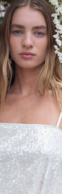 Model wearing a White Sequin Camisole Top with spaghetti straps, adorned with flowers in a beautiful outdoor setting.