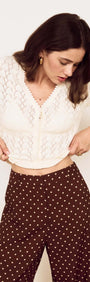 Woman adjusting her White Cotton Pointelle Knit Top, showcasing its feminine vibe and delicate details.
