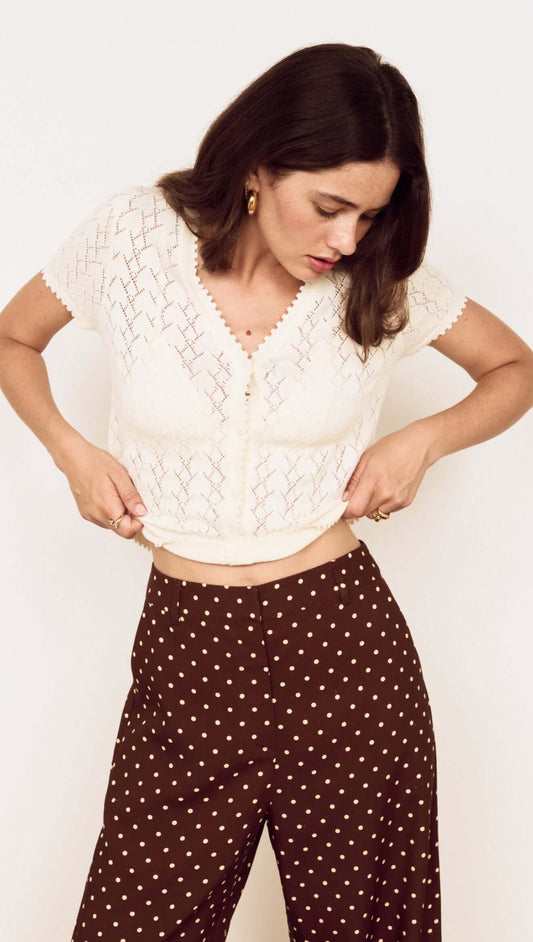 Woman adjusting her White Cotton Pointelle Knit Top, showcasing its feminine vibe and delicate details.