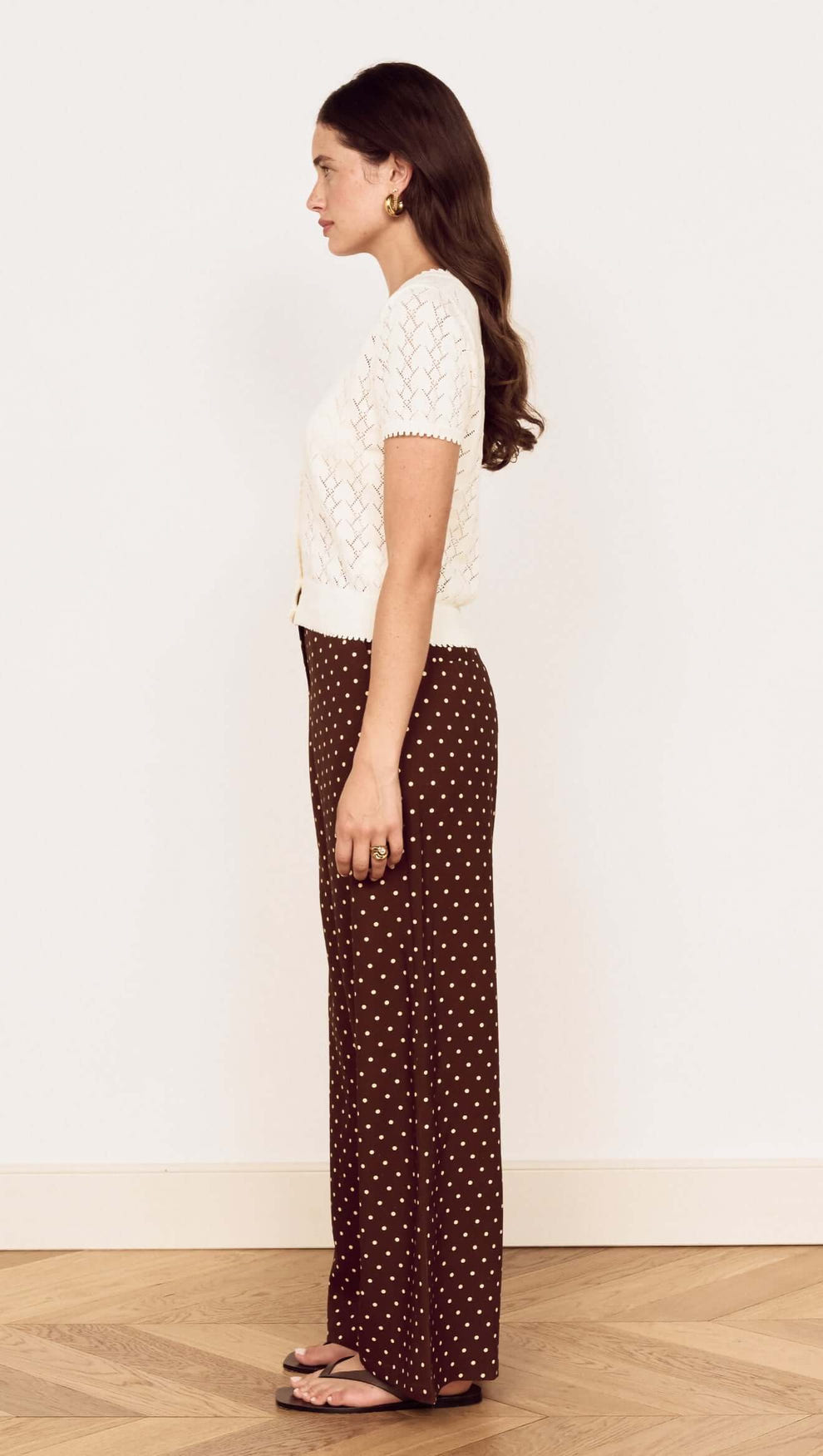 Model showcasing the White Cotton Pointelle Knit Top paired with brown polka dot pants, side view.