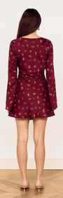 A woman wearing the Wine Satin Paisley Knot Front Bias Mini Dress, showcasing the back view with long flared sleeves.