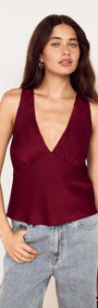 A model showcases the Wine Satin V-Neck Cami Top paired with denim, featuring a deep V-neckline and flared peplum hem.