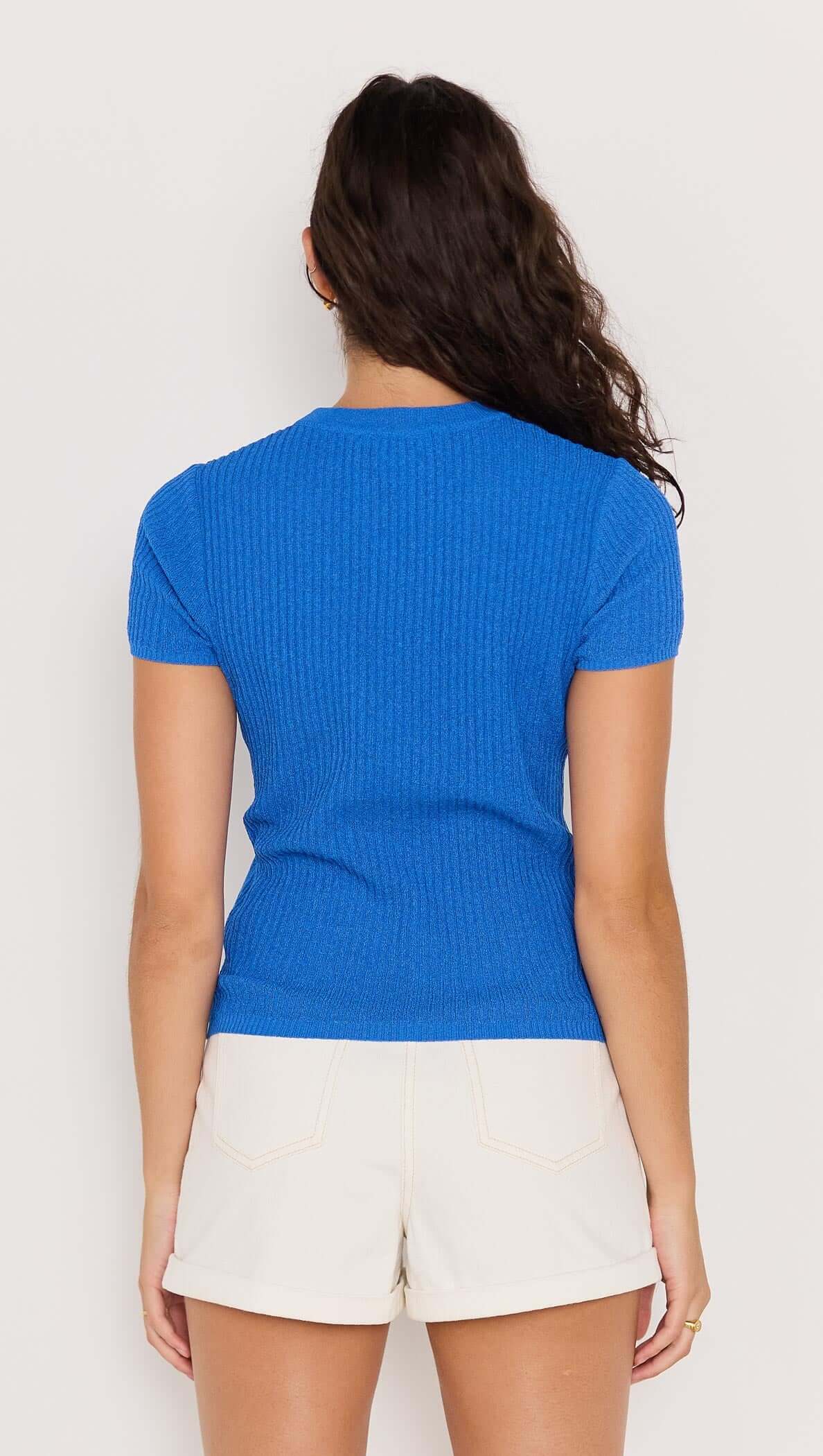Back view of a woman wearing a vibrant cobalt blue rib knit top paired with white shorts.