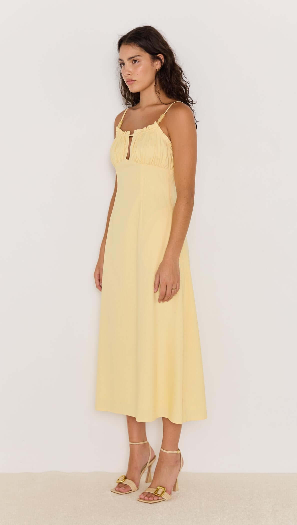 Model wearing a butter yellow bias cut midi dress with delicate straps and a flattering silhouette.