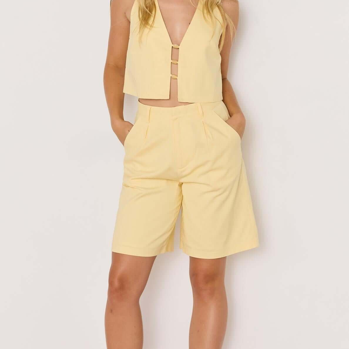 Model wearing a butter yellow high-waist Bermuda short with a matching crop top for summer style.