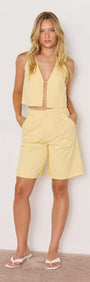Model wearing a butter yellow high-waist Bermuda short with a matching crop top for summer style.