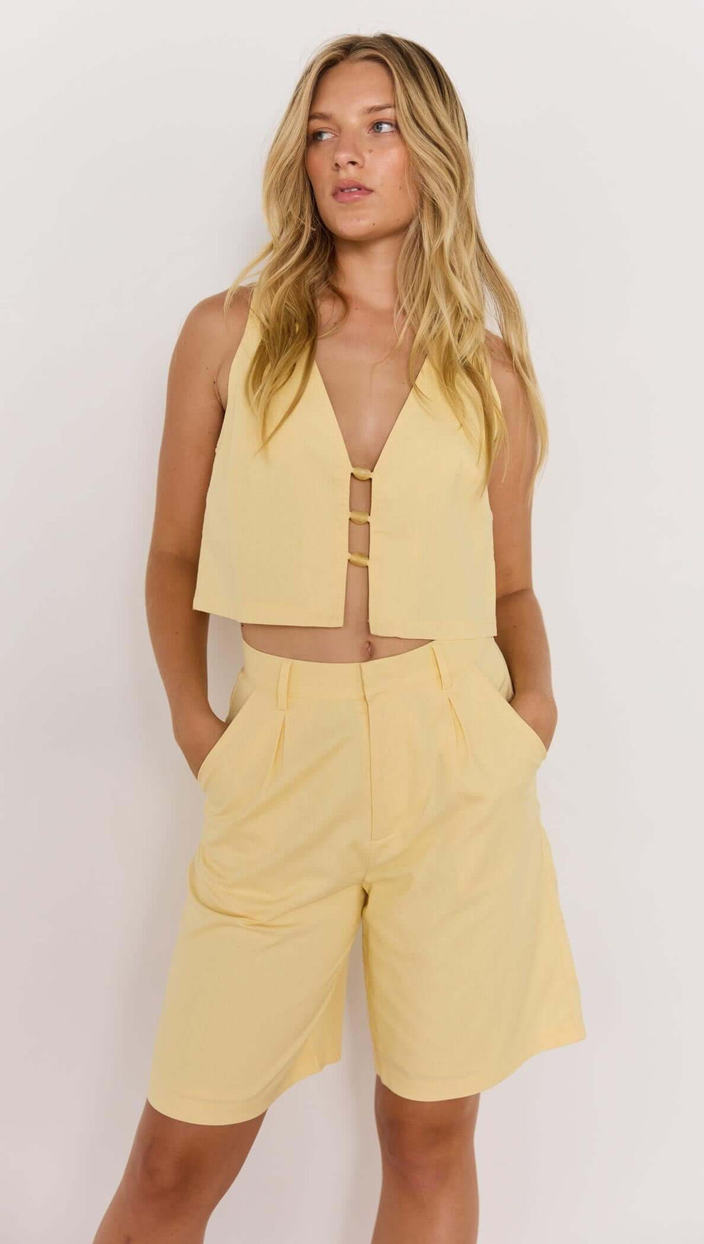 Model wearing a butter yellow high-waist Bermuda short and matching cropped top, stylish summer outfit.