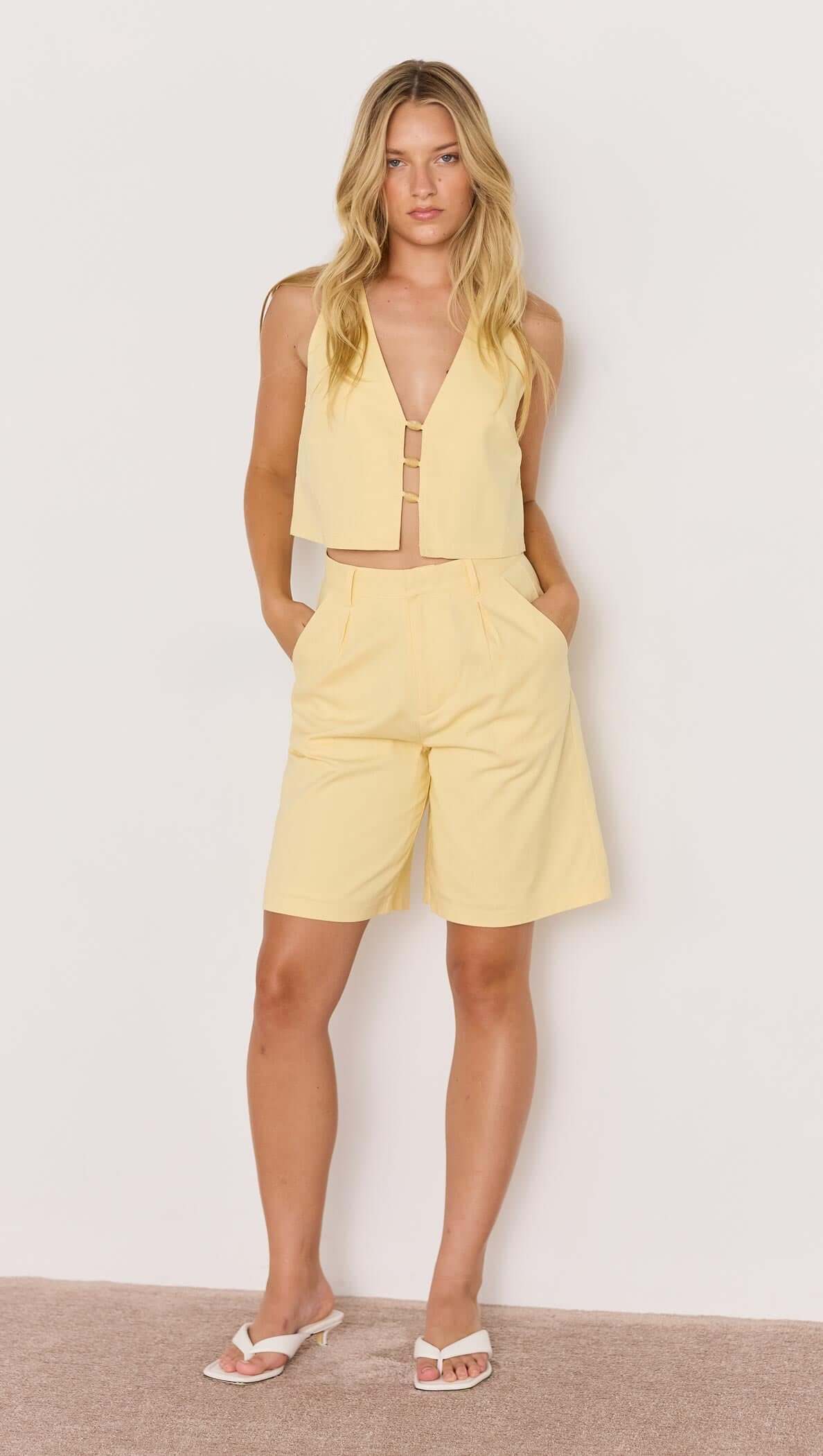 Model wearing a butter yellow high-waist Bermuda short with a matching crop top for summer style.