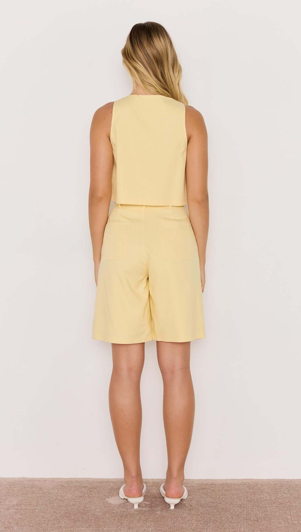 Back view of a model wearing Butter Yellow High-Waist Bermuda Shorts with a matching top, showcasing a breezy summer outfit.