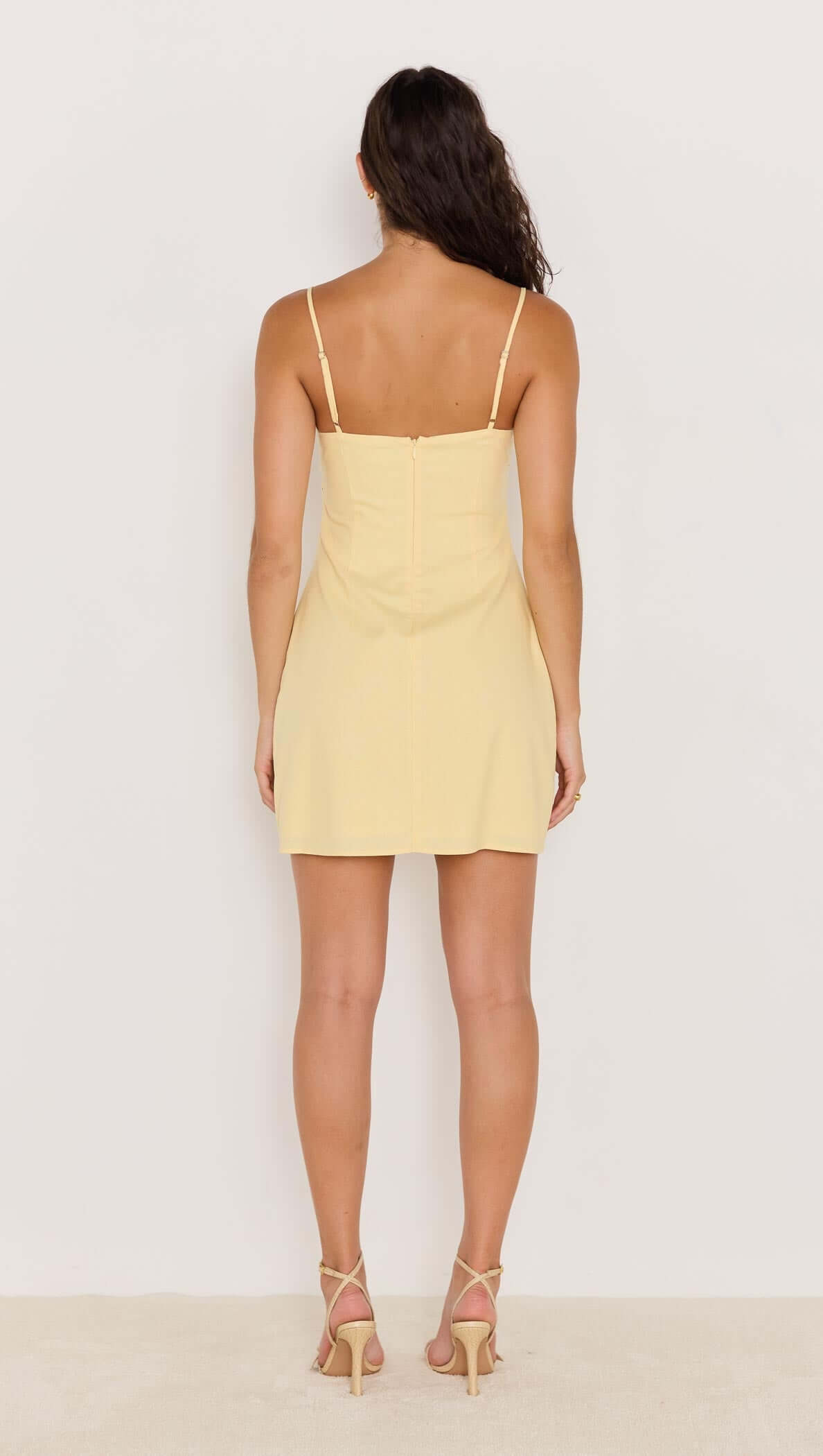 Back view of a model wearing a butter yellow mini dress with bead detail, showcasing adjustable straps and a fitted silhouette.