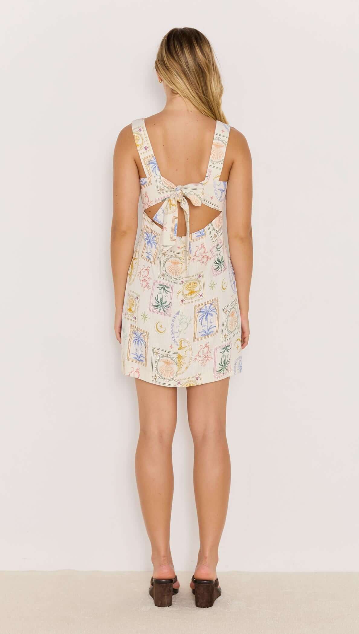 Back view of a printed tie-back mini dress featuring a square neckline and playful summer patterns.