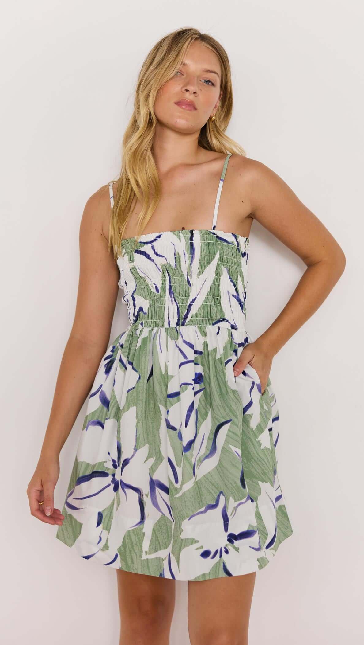Model wearing a green and white shirred mini dress with floral print and pockets, showcasing a stylish summer look.