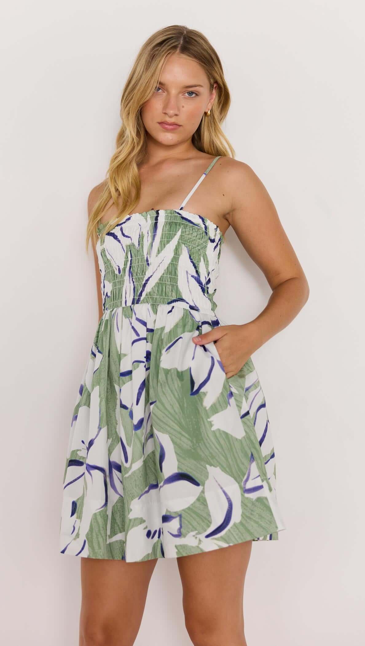 Model wearing a green and white shirred mini dress with floral print and pockets, perfect for summer outings.