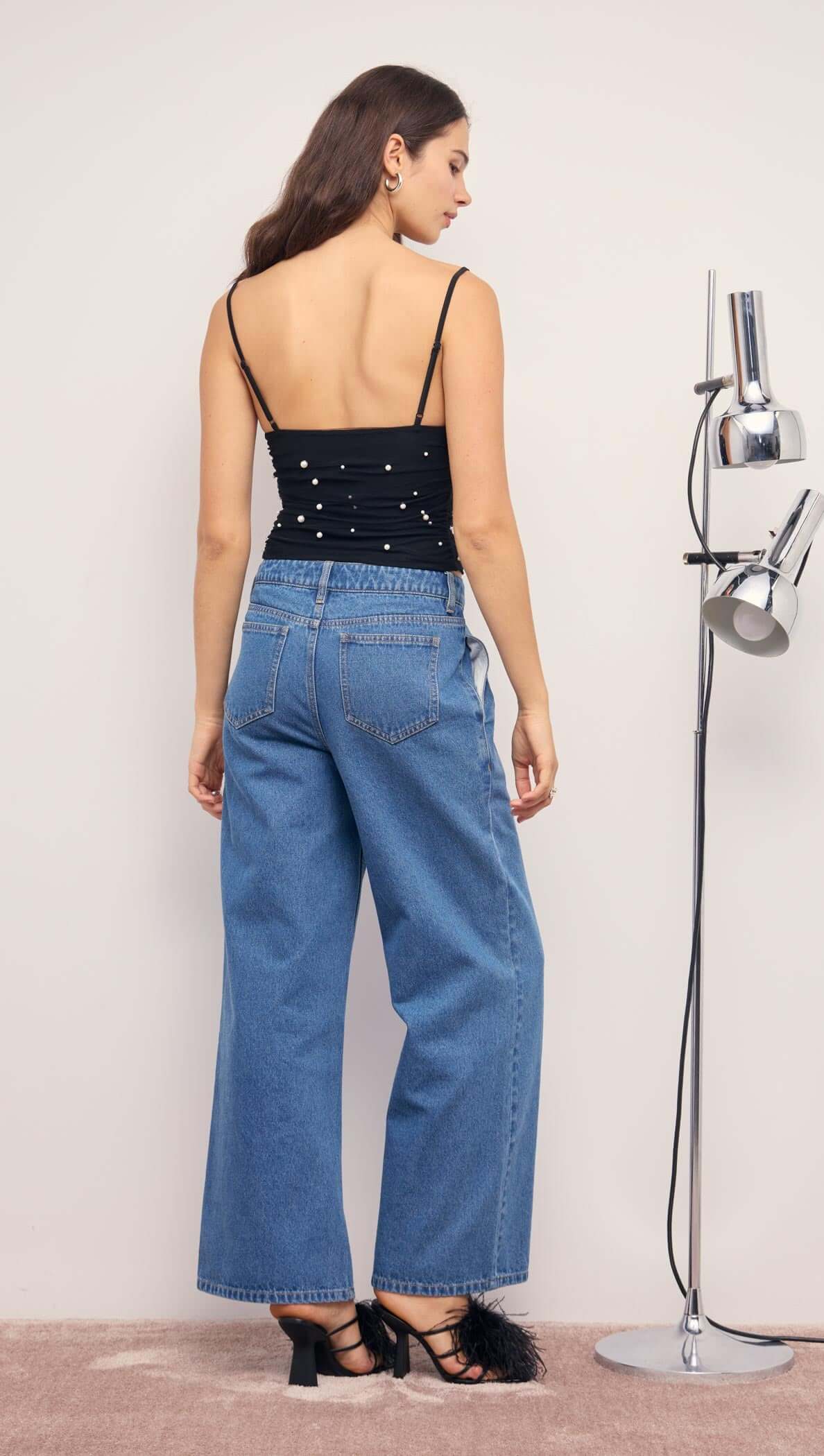 Back view of a model wearing a Pearl Embellished Black Mesh Crop Top with wide-leg denim pants.