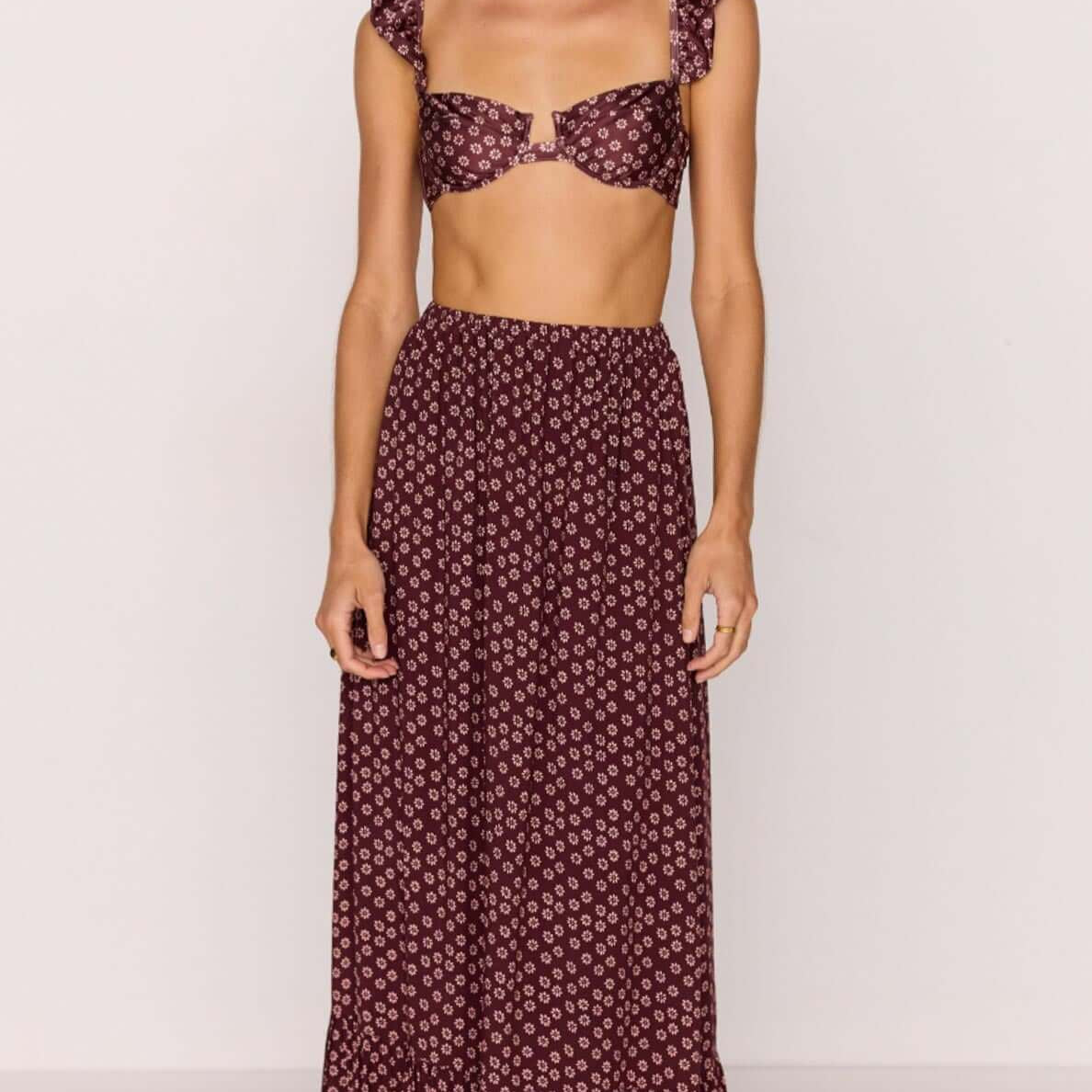Woman wearing a burgundy floral print ruffle hem maxi skirt with matching crop top.