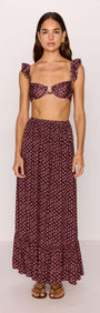 Woman wearing a burgundy floral print ruffle hem maxi skirt with matching crop top.
