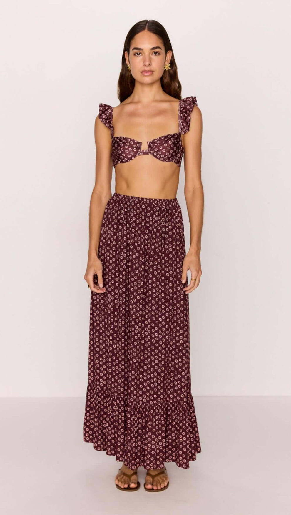 Woman wearing a burgundy floral print ruffle hem maxi skirt with matching crop top.