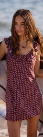 Model wearing a Burgundy Floral Print Ruffle Strap Low-Back Mini Dress at the beach, holding a towel.