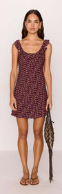 Model wearing a burgundy floral print ruffle strap low-back mini dress, holding a woven bag.