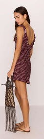 Model wearing a burgundy floral mini dress with ruffle straps and low-back, accessorized with a fringe bag.