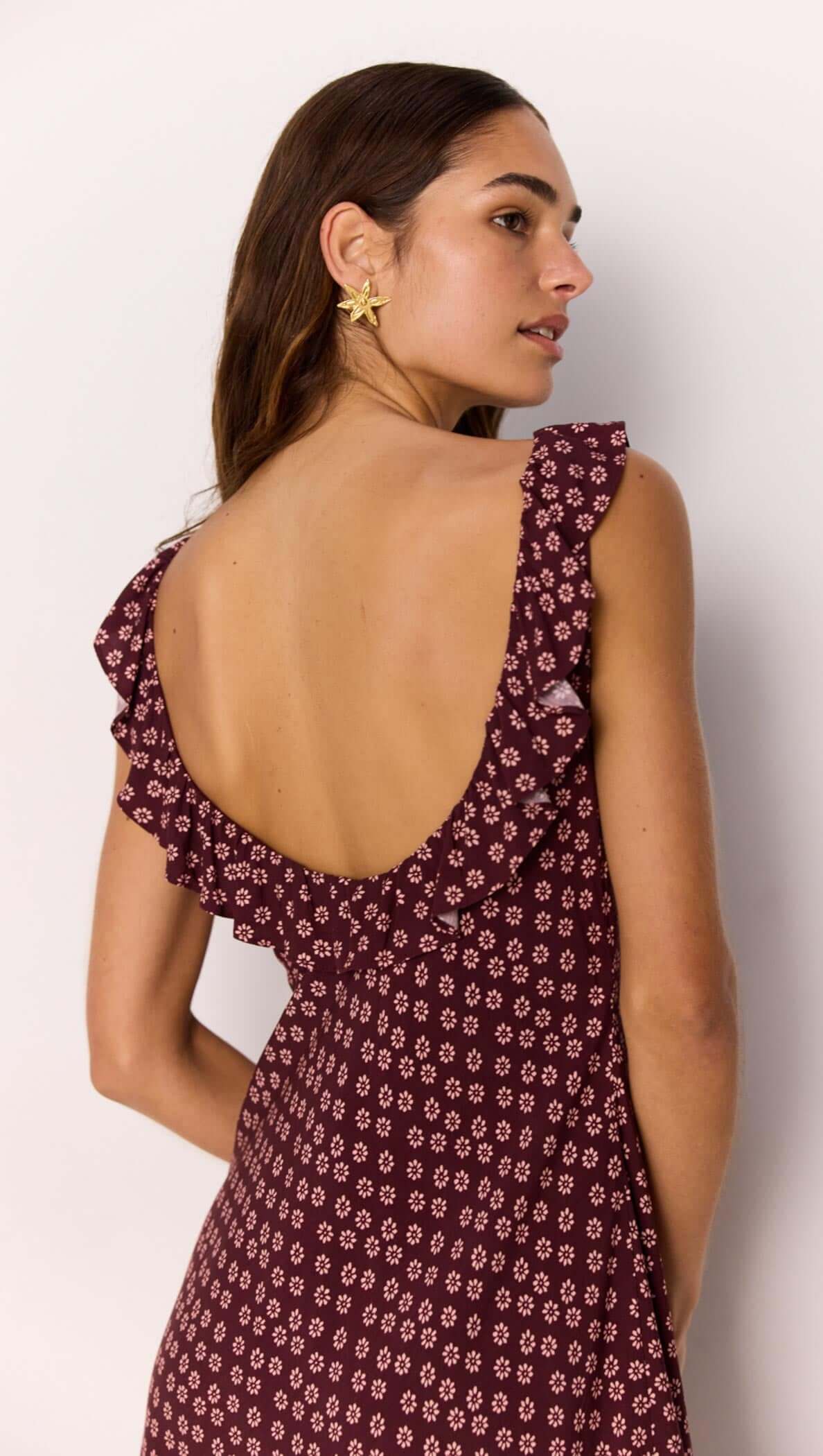 Model showcasing the back of a burgundy floral print mini dress with ruffle straps and a low back design.
