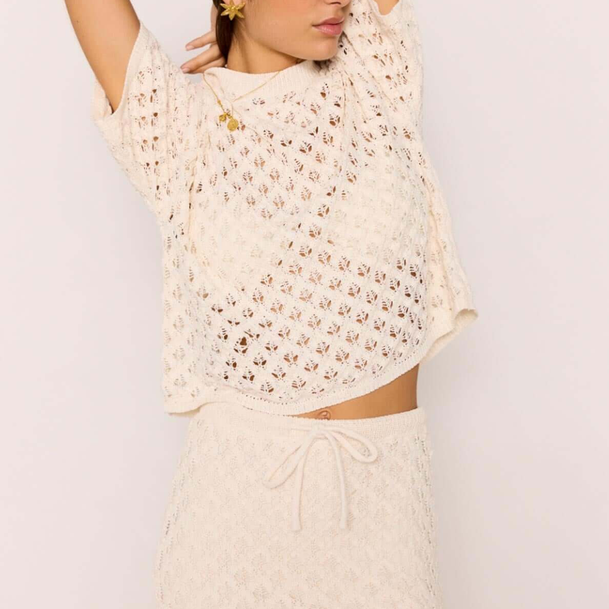 Woman wearing a White Pointelle Knit Mini Skirt with matching top, showcasing a cream open-knit design and ruffled hem.