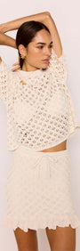 Woman wearing a White Pointelle Knit Mini Skirt with matching top, showcasing a cream open-knit design and ruffled hem.