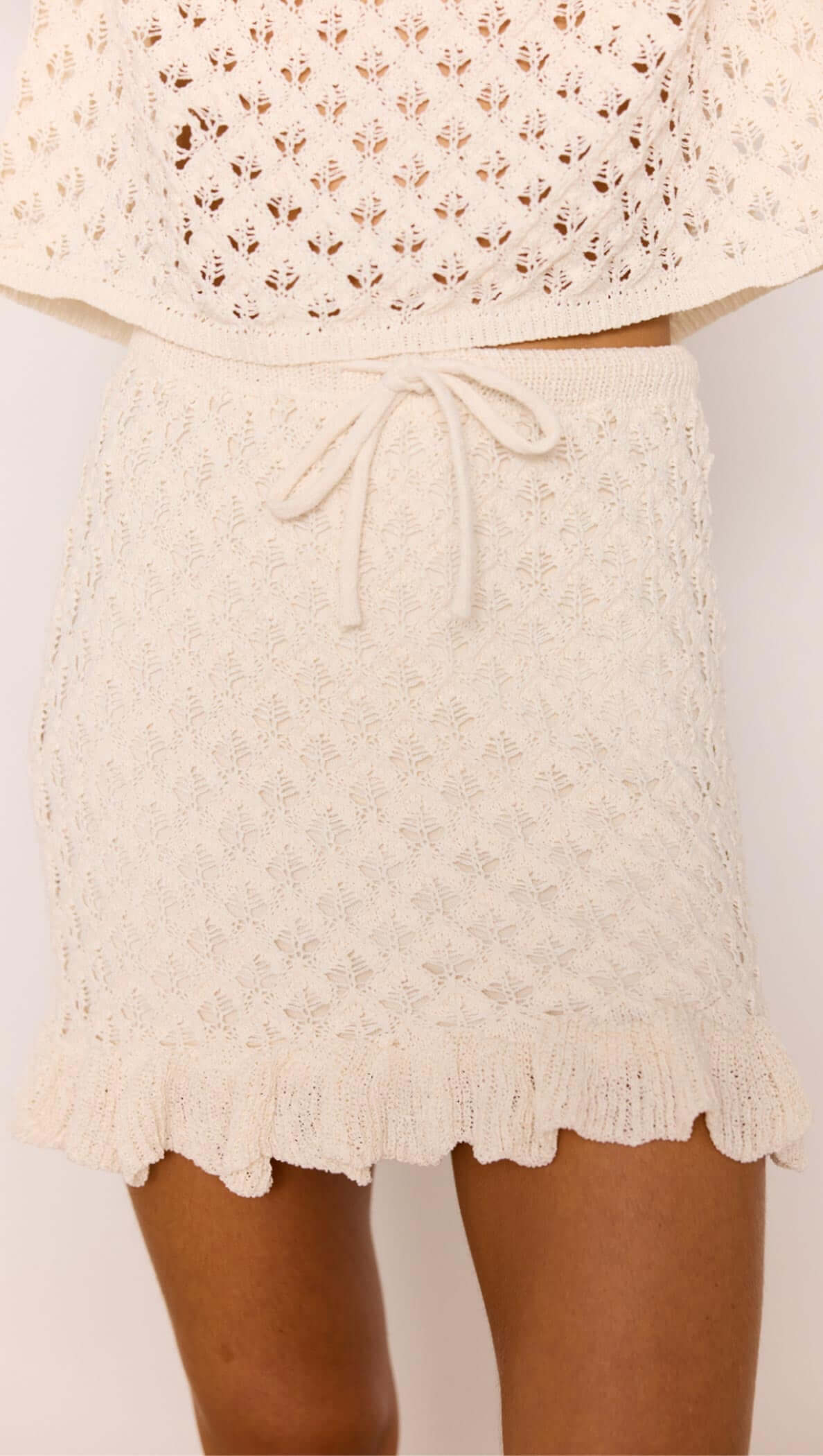 White Pointelle Knit Mini Skirt featuring a ruffled hem and elasticated waistband in cream color.