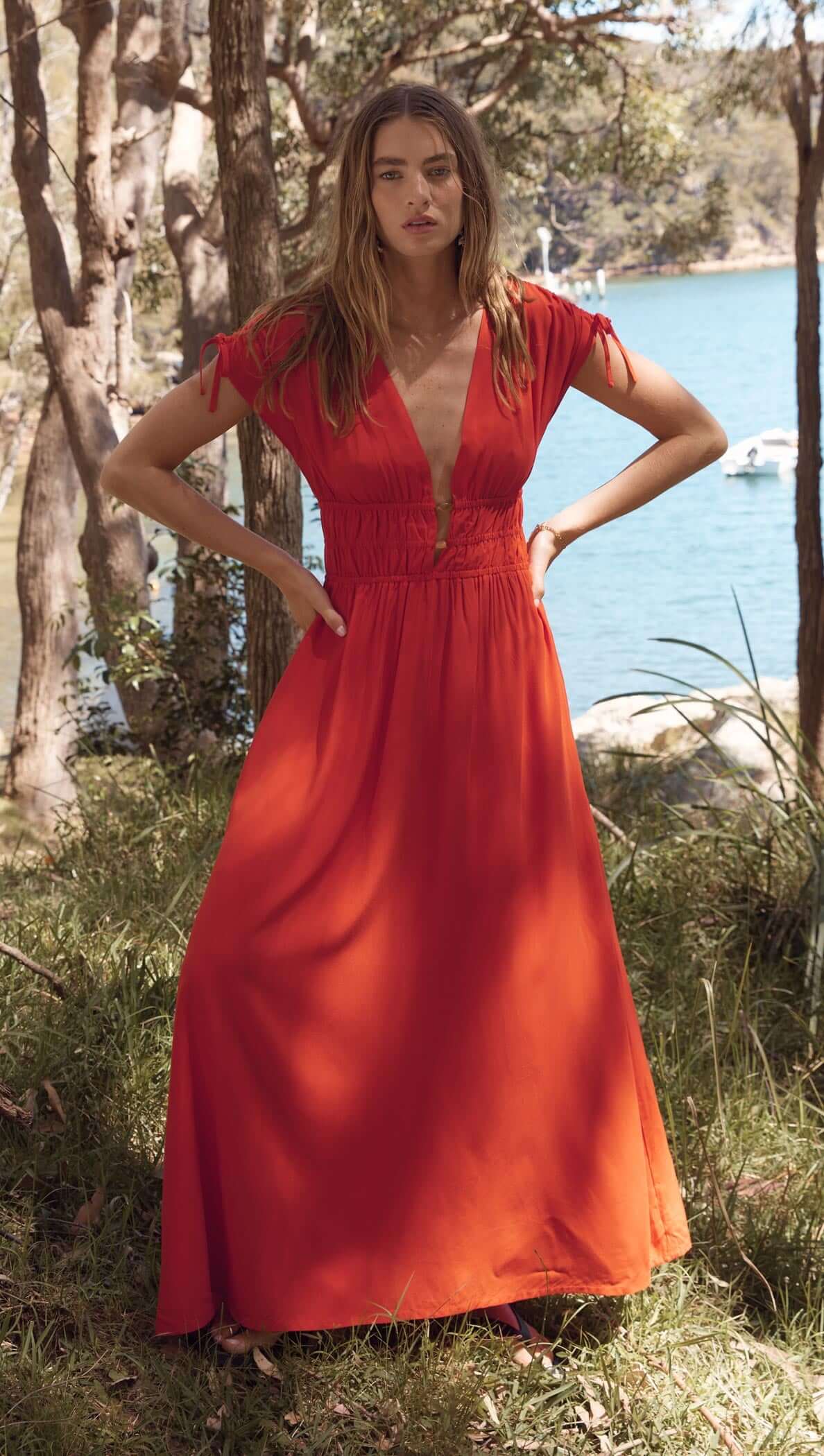 Scarlett V-Neck Midi Dress with Bead Detail in bright red worn by model near water and trees.