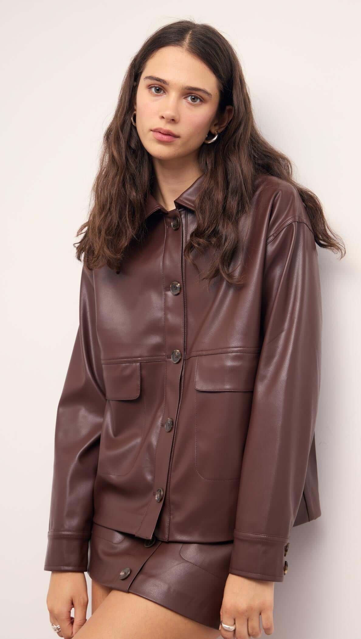 Model presenting the Brown Faux Leather Mini Skirt paired with a matching brown faux leather jacket.