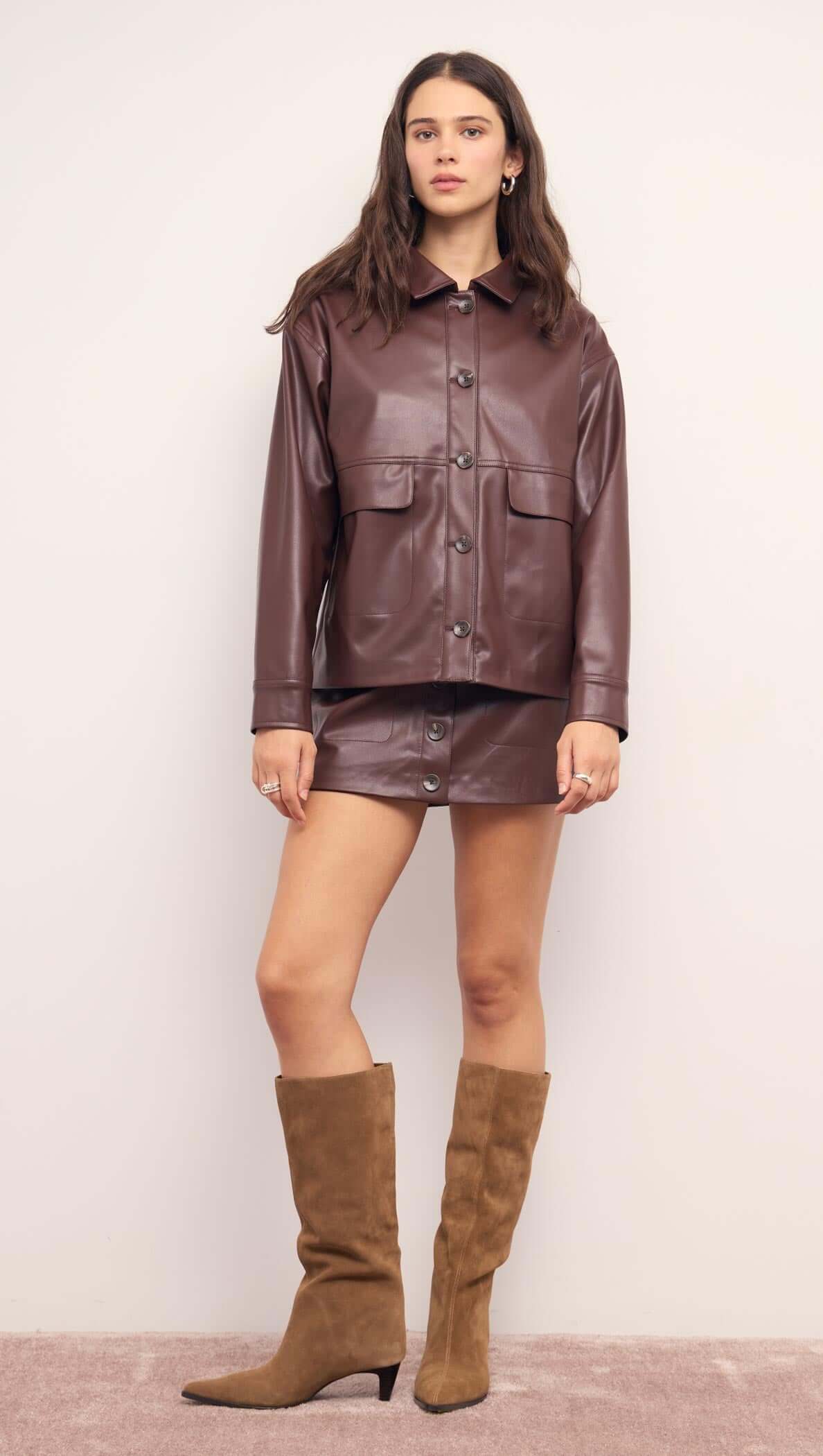 Model wearing a Brown Faux Leather Mini Skirt with a matching jacket and knee-high boots.
